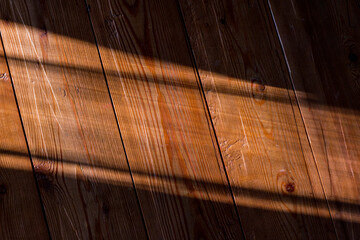 Old wooden wall surface with shadows. Wooden background under light of the morning or evening sun.