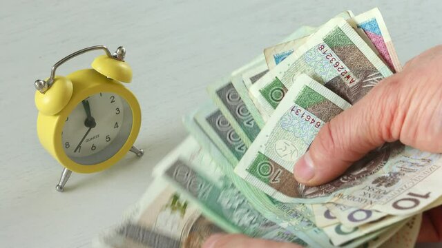 Polish zloty currency, Banknotes put on the desk next to the alarm clock set for five to twelve, time is money concept