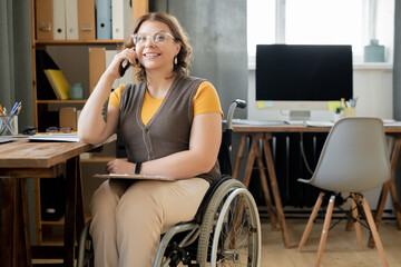 Happy young female agent or secretary in wheelchair consulting on mobile phone