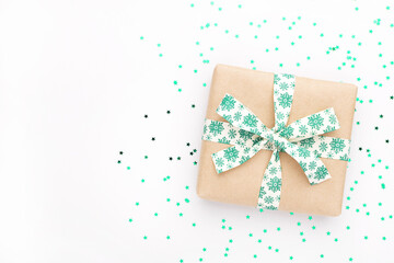 Christmas gift at gray background. New year flatly with craft present box, textile green ribbon and stars confetti.