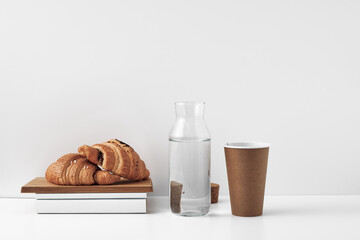 Croissants on a wooden board, a bottle with a cork stopper and a paper disposable glass on a white background. Natural and eco-friendly materials. Copy space, mock up.