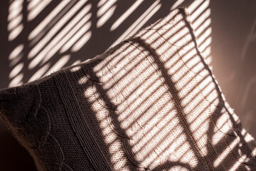Knitted pillow with blind shadows on the wall. Knitted pillow with jalousie shadows. Winter cozy...