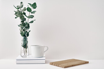 A mug, a stack of books, a wooden board and a transparent vase with eucalyptus branches. Eco-friendly materials in interior decor, minimalism. Copy space, mock up.