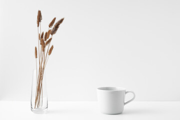 Mug and transparent vase with flowers on a white background. Eco-friendly materials in the decor of the room, minimalism. Copy space, mock up.
