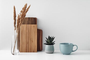 A mug, a potted houseplant, a clear vase and a wooden cutting board. Eco-friendly materials in the decor of the room, minimalism. Copy space, mock up.