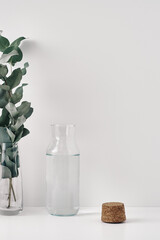 Two transparent vases, a eucalyptus branch, and a cork stopper on a white background. Copy space, mock up, top view.