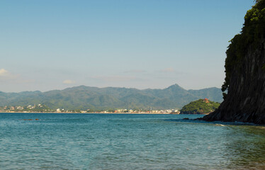 Beautiful landscape of the mexican pacific coast in a sunny day with trees, palms and green hills, some waves and cliffs with rocks