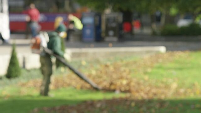 Blurred background shot of man blowing leaves in a park green, in slow motion 