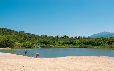 A group of people fishing in a mexican beach of the pacific coast  with a beautiful landscape in the background, and a clear and blue sky of a sunny day