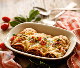 Baked vegetarian enchiladas stuffed with vegetables, sprinkled with cheese and herbs, served in a baking dish close-up view
