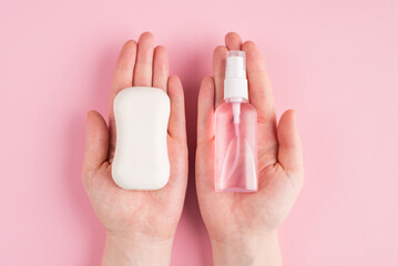 Top above overhead pov first person close up view photo of hands holding soap and sanitizer isolated on pastel pink color background with copyspace