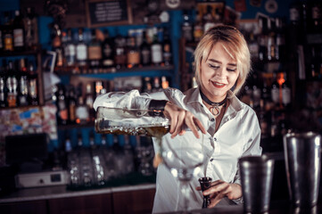 Charming woman bartending formulates a cocktail while standing near the bar counter in pub