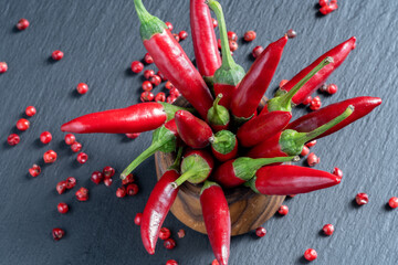 A bunch of red hot chili peppers in a wooden stand. Cayenne peppers and red peppercorns on a black...