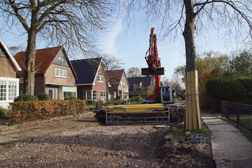 Roadwork with a red, green excavator in the Dutch village of Bergen. Wood boards placed around the...