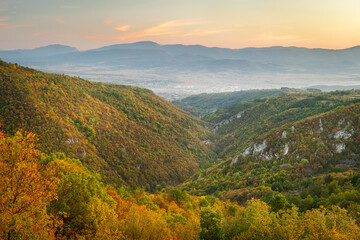Obraz premium Autumn colored trees around the rocky canyon of Gradasnica river, leading towards misty, hazy Pirot cityscape and colorful blue hour sky