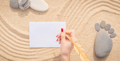 Fototapeta na wymiar Arrière-plan grains de sable de mer, sable fin de plage avec enveloppe et coquillages. Main féminine qui écrit sur une enveloppe. Emplacement pour texte sur papier. 