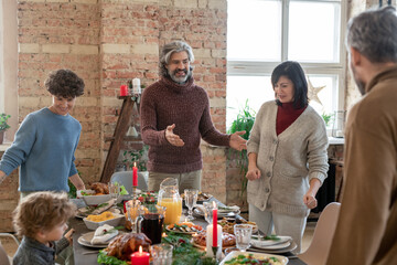 Happy mature man in casualwear helping family members to take their places