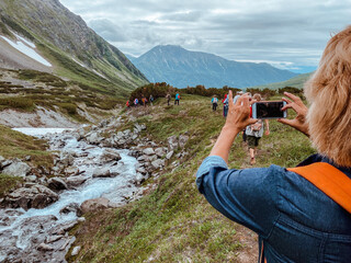 A woman with a phone in her hands takes a photo of tourists on a mountain trail while trekking