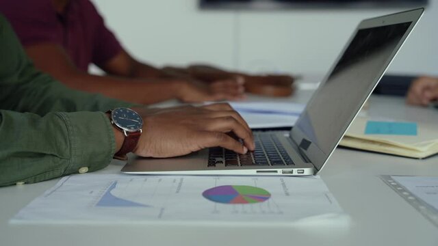 Male accountant checking pie charts logging in figures onto spreadsheet on laptop sitting in conference room