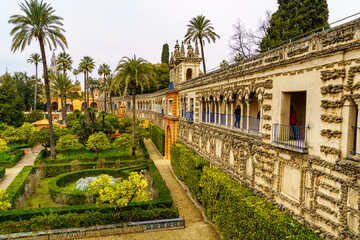 Obraz premium Jardín exterior de palacio andaluz en Sevilla con plantas ornamentales verdes y arquitectura árabe antigua con arcos y balcones.
