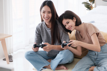 Two Asian teenage girls are Intimate friends with short and long hair smiling and playing video games in the bedroom. Young women are enjoying leisure activities.