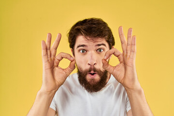 Bearded man emotions fun gesture with hands white t-shirt close-up yellow background