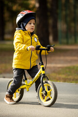 Cute little boy in protective helmet riding balance bicycle along asphalt road