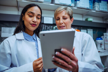 Senior pharmacist teaching young student how to use the digital tablet to locate medicine standing in pharmacy 