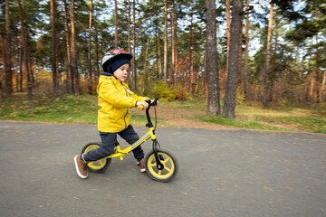 Obraz premium Sportive little boy in casualwear and safety helmet riding on balance bicycle