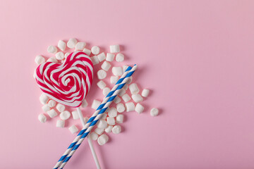 Heart-shaped lollipop and white sweet marshmallows on pink background