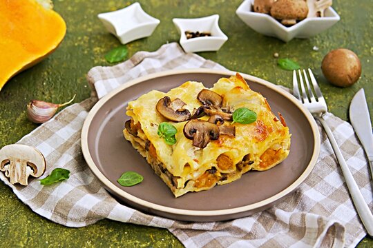 A serving of lasagna with pumpkin and mushrooms on ceramic plate on olive concrete background. Lasagna recipes. Pasta recipes.