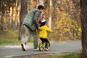 Rear view of young man running after his active little son riding balance bike