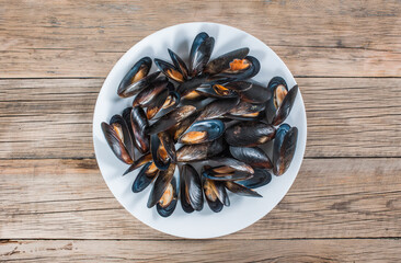 Many sea mussels in shells on a white plate on an old wooden background. View from above