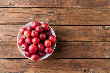 Overhead shot of organic plums in bowl on wooden background with copyspace