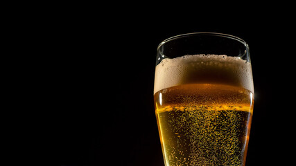 Close-up of fresh frothing light beer in a glass on a dark background