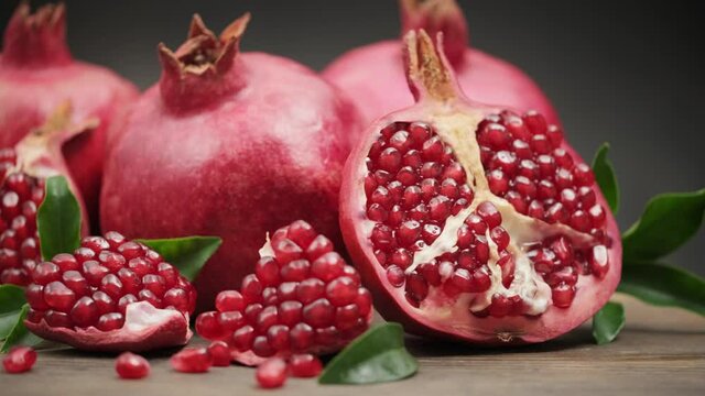 Ripe red pomegranates and one cut in half with a leaf on a wooden board on a dark background. Slider shot 4K UHD