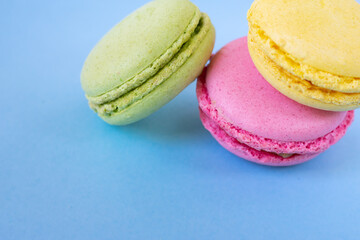 Yellow, pink and green macarons in the corner on blue background. Traditional french almond biscuits