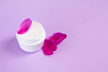 Soft cream for skin care in white jar with peony petals on pink background