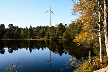 Obraz premium Beautiful Lake Blindensee in the Black Forest, Germany during autumn with its dark, clear water and the wind power station and forest reflecting in it.