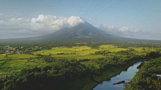Hillside river at erupt volcano with green grass shore at Philippines countryside aerial. Fields, valley, meadows of nobody nature landscape. Cinematic scenic of Mayon mount erupt at mist haze