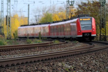 Fototapeta na wymiar Gleisbett mit Gleisschotter und Schienenstrang und Nahverkehrszug auf freier Strecke in einer Kurve im Herbst - Stockfoto