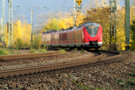 Gleisbett mit Gleisschotter und Schienenstrang und Nahverkehrszug auf freier Strecke in einer Kurve im Herbst - Stockfoto