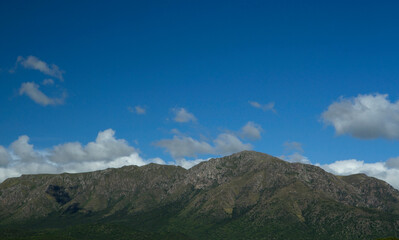 Beautiful view of landmark Uritorco hill in Capilla del Monte, Cordoba, Argentina. The rocky mountain peak and green forest under a deep blue sky in a sunny summer day. 