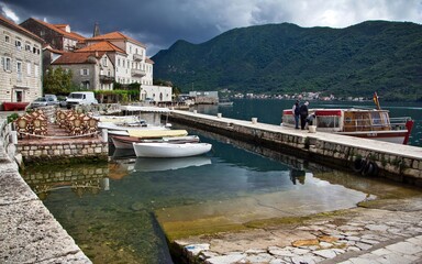An embankment with medieval stone houses of the Bay of Kotor in Perast, Montenegro. Two people...