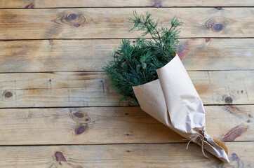 Winter rustic bouquet with fir branches. Branches of Christmas tree in the kraft paper on a wood background, zero waste. Christmas bouquet top view. Eco friendly packaging, gift.