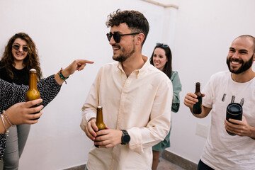portrait of party teens drinking and laughing. One of them is in the center and a girl points to it. The others laugh. Another teenager also appears with the loudspeaker in his hand
