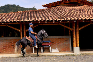 Man riding a horse next to the stable de la equine farm. Man galloping outdoors. Lifestyle.