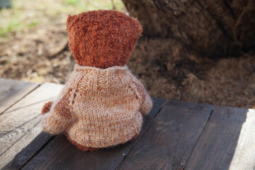 lonely brown teddy bear in a sweater sitting on wooden planks