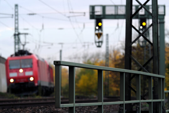 Signalbrücke der Bahn und herannahender Zug mit roter Lok auf freier Strecke in einer Kurve im Herbst - Stockfoto