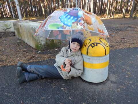 A child in a city park under an umbrella next to a concrete protective column